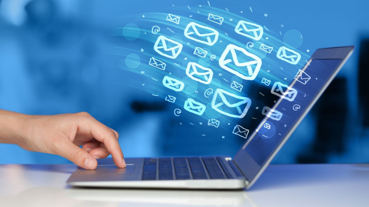Hand on laptop keyboard with illustrated email icons emerging from the screen, symbolizing targeted communication and outreach in cybersecurity email marketing campaigns.